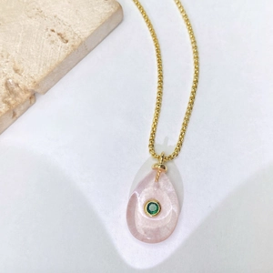Détail du pendentif goutte en cristal rose avec zircon vert sur une chaîne dorée