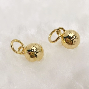 Macro shot of polished gold spherical pendants with rings on white plush background