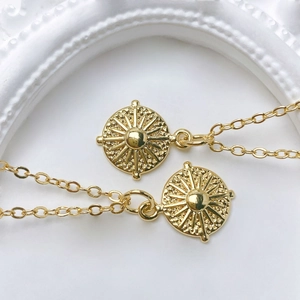 Macro detail of sunburst charm pendants in polished gold plating with fine link chains