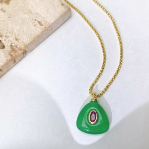 Vue macro d'un pendentif goutte verte avec pierre violette et chaîne dorée sur pierre