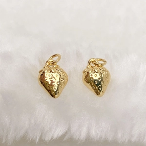 Macro shot of gold strawberry pendants on white faux fur background for jewelry making