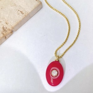 Détail d'un pendentif ovale doré avec pierre rouge et zircon central sur une chaîne