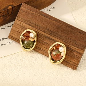 Detalle de pendientes vintage con piedra verde y perla sobre un fondo de madera