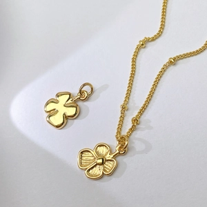 Detail von goldenen Blumenanhängern und Perlenhalskette mit polierter Metalltextur