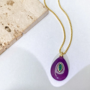 Vue détaillée du pendentif goutte violette avec zircon vert sur une chaîne dorée