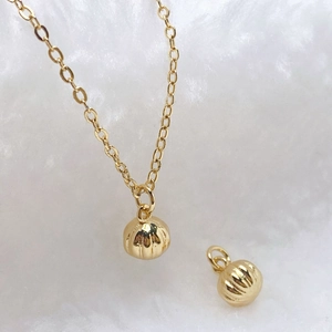 Macro shot of gold-plated ribbed ball pendants and fine chain on white cotton background