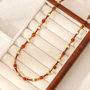 Primer plano de collar de cuentas rojas y crema con detalles dorados en un estuche
