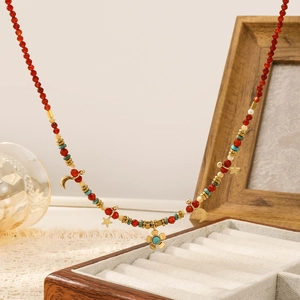 Detalle de collar de cuentas rojas con colgantes de estrella y luna dorados sobre fondo
