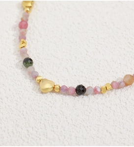 Detalle macro de cuentas de turmalina multicolor y colgante de corazón dorado en el collar