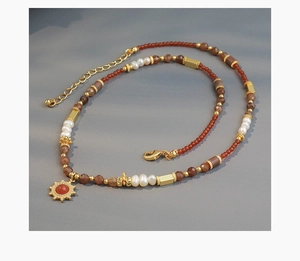 Detail of beaded necklace with freshwater pearls, red stone beads and golden sun pendant