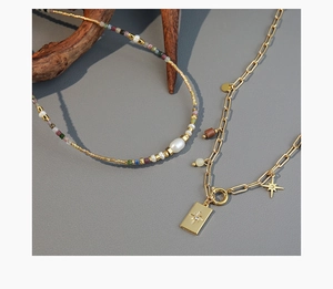 Dettaglio della collana di perline colorate e catena a graffetta dorata con ciondoli a stella