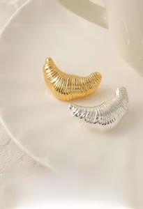Macro shot of silver and gold croissant-shaped brass brooches on a ceramic tray