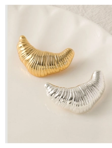 Close-up of silver and gold irregular croissant brooches with textured metallic spiral design
