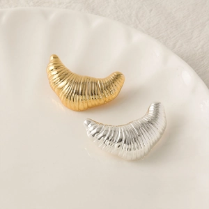 Irregular croissant brooch in silver and gold with textured metal finish on white plate