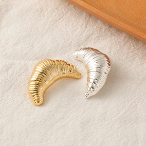 Irregular croissant-shaped metal brooches in gold and silver finish on a linen base