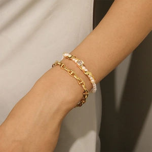 Detalle de pulsera de cadena de ancla dorada y perlas con circonita cuadrada