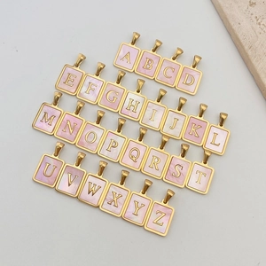 Makroaufnahme von 26 quadratischen Gold-Alphabet-Anhängern mit rosa Muschelstruktur