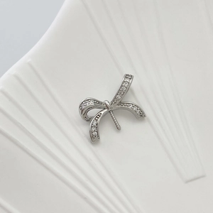 Macro shot of silver bow pendant with micro-paved zircons on white ceramic texture