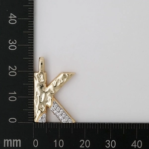 Close-up of golden letter K pendant with cubic zirconia and hammer finish texture