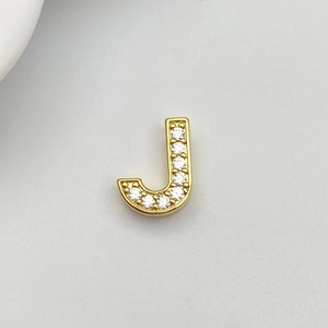 Detailed macro view of gold-plated J-shaped pendant with white cubic zirconia stones