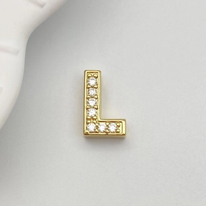Detailed close-up of golden metal letter L charm with sparkling white zircon inlays