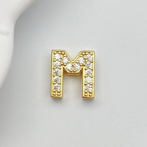 Detailed macro view of gold-plated letter M charm with pave white cubic zirconia crystals
