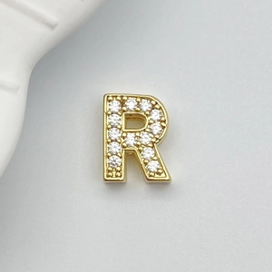 Macro detail of the letter R jewelry charm with sparkling white zircons in 18K gold finish