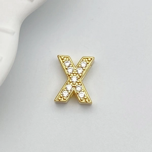 Macro detail of a gold letter X charm with white cubic zirconia for DIY jewelry