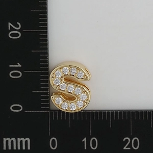 Detail shot of a gold-tone 'S' letter charm with micro zircons next to a ruler