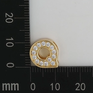 Detail view of 11mm gold letter Q charm with white zircon stones on a scale ruler