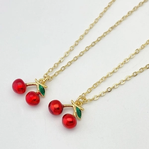 Détail de pendentifs cerises rouges avec feuilles vertes sur de fines chaînes dorées