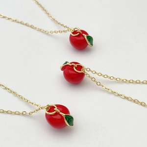 Détail de trois chaînes dorées avec pendentifs pomme rouge mignons et feuilles en émail
