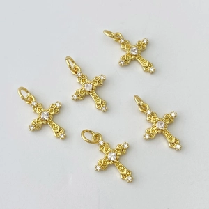 Gros plan de cinq pendentifs croix baroques dorés sertis de zircons sur fond gris