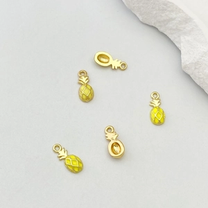 Détail macro de breloques ananas en métal doré et émail jaune pour la création de bijoux