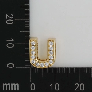 Macro shot of 11x13mm gold plated letter U pendant with white zircon stones on a scale