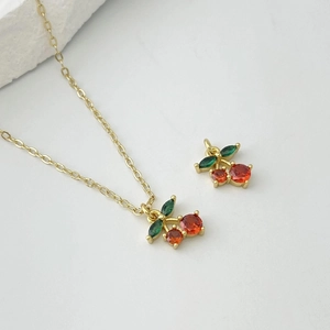Golden cherry pendant necklace with red and green zircon crystals on a white background