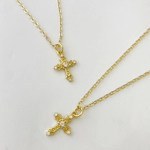 Gros plan détaillé de deux pendentifs croix dorés avec zircons micro-pavés sur fond blanc