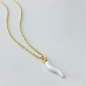Detailed macro view of a gold-plated necklace featuring a white resin cornicello pendant