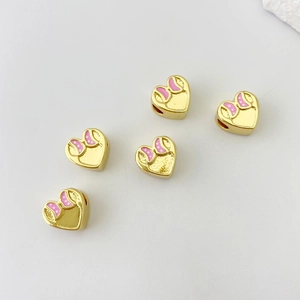 Dettaglio macro di perline a cuore dorate con smalto rosa e fiocchi a pois bianchi fai da te