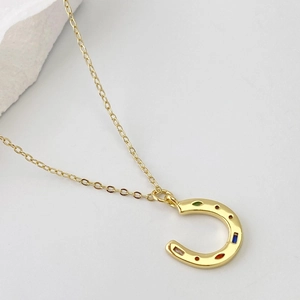 Collier fer à cheval doré chic avec zircons colorés sur un fond blanc épuré