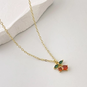 Close-up of golden cherry pendant with vibrant red gemstones and green crystal leaves