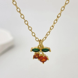 Macro view of gold cherry pendant necklace with red round stones and green marquise leaves
