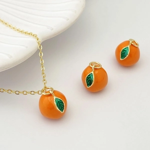 Détail des breloques en forme d'orange avec feuilles vertes et collier doré fin