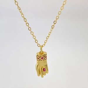 Gros plan du pendentif main vintage doré avec zircons rouges et détails ajourés