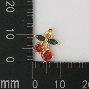Macro shot of cherry pendant with red round stones and green marquise leaves next to ruler