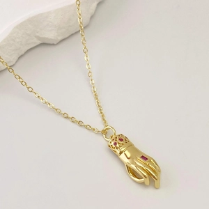 Détail macro d'un pendentif en forme de main dorée avec zircon rubis sur une chaîne croisée