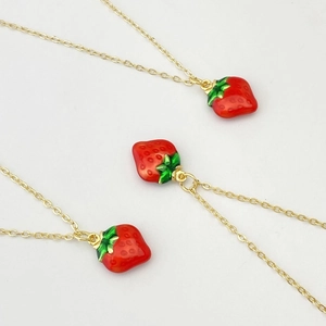 Détail de trois colliers avec pendentifs fraises mignons en émail rouge et vert