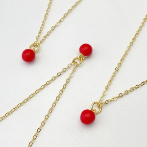 Gros plan de colliers à chaîne dorée fine avec pendentifs en perles rouges sphériques