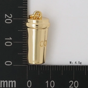 Vue macro d'un pendentif tasse à café doré montrant les dimensions sur une règle graduée
