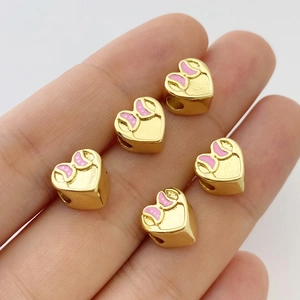 Dettaglio charm cuore dorato con fiocco rosa a pois tenuto in mano per dimensione